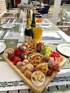 a wooden tray topped with waffles and fruit next to bottles of wine on top of a table