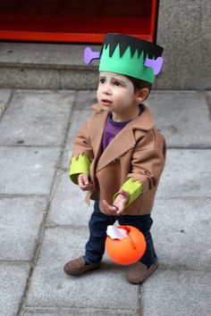 a young boy wearing a costume and holding an orange ball on the sidewalk with his hands