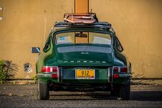 an old green car is parked in front of a building with luggage on top of the roof