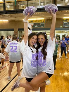 two young women holding up their hands in the air while standing on a basketball court