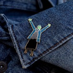 a lapel pin depicting a man with his arms in the air, on a blue jean jacket