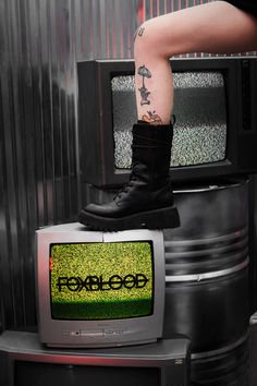 Black boots standing on top of an old CRT with a yellow/green tv static screen showcasing the FOXBLOOD logo Platform Boots, Fashion Inspo