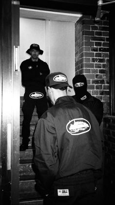 two men in black jackets and hats standing on the stairs with their backs to each other