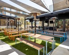 an outdoor seating area with wooden benches and tables on artificial grass in the foreground