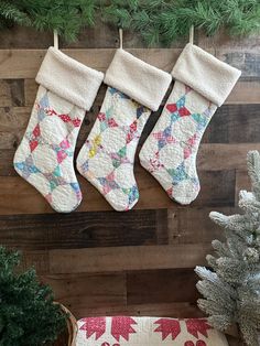 three quilted christmas stockings hanging on a wooden wall next to a potted plant