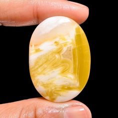 a hand holding an oval shaped yellow and white marble