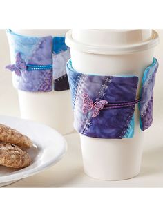 two coffee mugs and some cookies on a white plate next to a drink cup