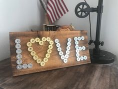 a wooden sign that says love spelled out with buttons and an american flag in the background