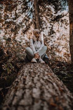 a woman sitting on top of a tree trunk in the middle of a wooded area