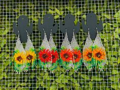 four pieces of bead art with flowers on them are hanging from a wire mesh fence