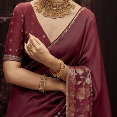 a woman in a maroon sari with gold jewelry on her neck and hands clasped together