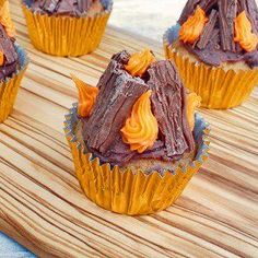 cupcakes with chocolate frosting and orange icing on a wooden tray next to water