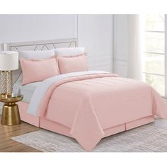 a bed with pink sheets and pillows on top of it in a room next to a lamp