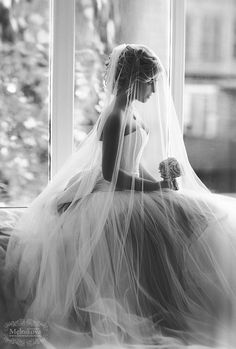 a woman sitting on top of a bed wearing a wedding dress and holding a bouquet