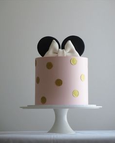 a pink cake with gold polka dots and mickey mouse ears on top, sitting on a white pedestal