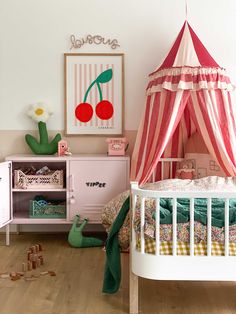 a child's bedroom with pink and white furniture, striped canopy bedding, green toys