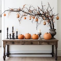 a wooden table topped with lots of pumpkins next to a vase filled with candles