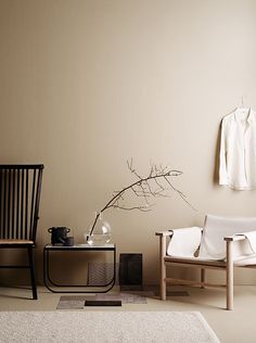 a room with two chairs, a table and a vase on the floor in front of a white wall