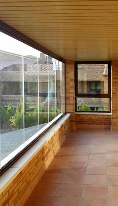 an empty room with large windows and tiled flooring on the outside wall, looking out onto a courtyard