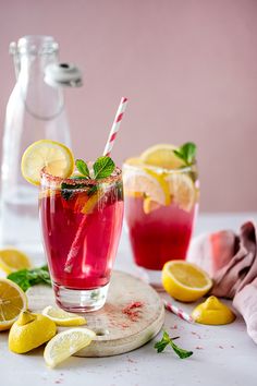 two glasses filled with pink lemonade and mint garnish next to sliced lemons