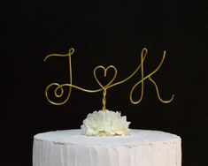 a white cake topped with a gold monogram topper and a flower on top