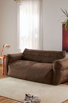 a brown couch sitting on top of a hard wood floor next to a potted plant