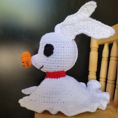 a crocheted white dog with a carrot in its mouth sitting on a chair