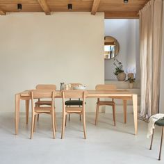 a dining room table and chairs in front of a white wall with wood beams on the ceiling