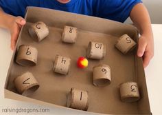 a young boy holding a cardboard box filled with toilet paper roll numbers and an orange ball