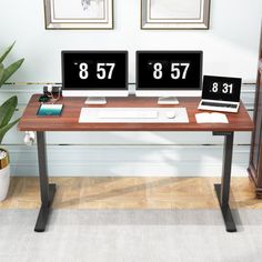 two computer monitors sitting on top of a wooden desk next to a potted plant