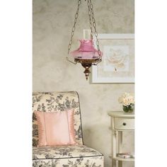 a pink lamp hanging from the ceiling next to a chair and table with flowers on it