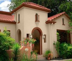 an orange house with red tile roofing and green plants in front of the building