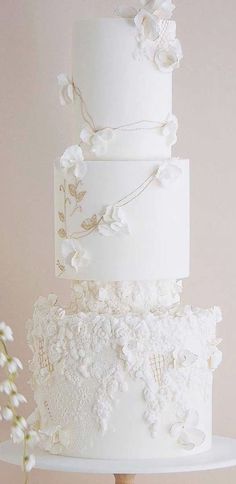 a three tiered white wedding cake on top of a wooden table next to a vase with baby's breath flowers