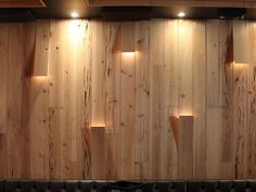 a black leather couch sitting in front of a wooden wall with three lights on it