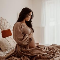 a pregnant woman sitting on a bed with her arms folded over her stomach and looking down