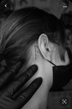 a woman with black gloves on her head and behind her ear is a tattoo that reads,