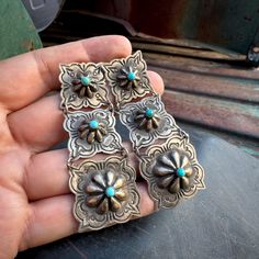 Here we have a striking pair of sterling silver earrings made of three squareish repousse conchos in graduated sizes, connected with jump rings, each super light and articulating, forming a sort of ladder chandelier. The first section is the smallest, with stamped border and a small dot of turquoise at the tip of the repousse concho shape that has been pounded out from the other side. Next is a slightly larger middle section, then the largest third one--each with dots of turquoise and each with Ladder Chandelier, Native Necklace, Native American Earrings, Native American Rings, Old World Style, Metal Stamping, Jump Rings, Chandelier Earrings, Sterling Silver Earrings