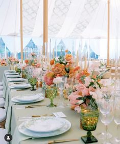 a long table with white plates and pink flowers in vases on the tables set for an event