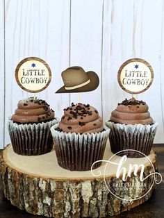 three cupcakes with brown frosting and cowboy hats are on a tree stump