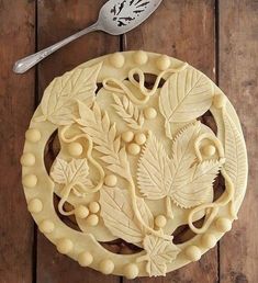 a cookie decorated with leaves and berries on top of a wooden table next to a spoon