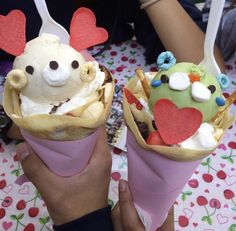 two ice cream cones with faces and hearts on them are being held up by someone's hands