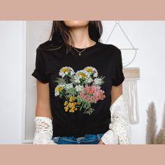 Introducing our Wildflowers T-Shirt, a blossoming beauty that captures the essence of nature's vibrant colours. This floral-inspired tee is designed for ladies who appreciate the delicate charm of wildflowers. It's the perfect gift for women, whether it's for your best friend or a dear friend who loves floral motifs. Our premium t-shirt is crafted with utmost care, ensuring both comfort and softness. Made from 100% cotton, it offers a luxurious feel against your skin. The heather colours feature a blend of 52% cotton and 48% polyester, combining durability and style in one. Fabrication: *Solid colours: Crafted with 100% cotton for a luxurious feel *Heather colours: Blending 52% cotton and 48% polyester for durability and comfort *Light fabric material that runs true to size, providing a pe Spring Black T-shirt With Floral Print, Casual T-shirt With Floral Embroidery For Gift, Botanical Floral Print Relaxed Fit T-shirt, Black Floral Print T-shirt For Spring, Spring Botanical T-shirt With Floral Design, Spring Botanical Graphic Print T-shirt, Spring Floral Print Graphic Tee, Spring Botanical Flower T-shirt, Black Botanical Top For Spring