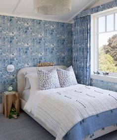 a bedroom with blue floral wallpaper and white bedding in front of a window