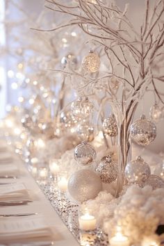 a table topped with lots of white christmas ornaments and trees covered in snow next to candles