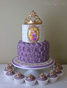 there is a purple and white cake with princesses on it, surrounded by cupcakes