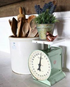 an old kitchen scale is sitting on the counter next to utensils and a potted plant