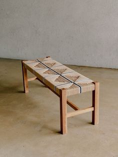 a small wooden bench sitting on top of a cement floor next to a white wall