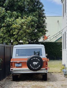 an orange and white jeep parked in front of a house with a black tire cover