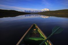 a green canoe is in the water with mountains in the backgrouds and blue sky