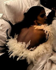 a woman laying in bed with feathers on her back